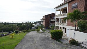 A residential building with a stone pathway, green lawns, and a view of the sea. - Hidden Hills 2A Ocean View Valley Church Rd (Jolly harbour)