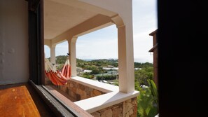 A balcony with a stone wall, a hammock, and a view of a green landscape. - Hidden Hills 2A Ocean View Valley Church Rd (Jolly harbour)