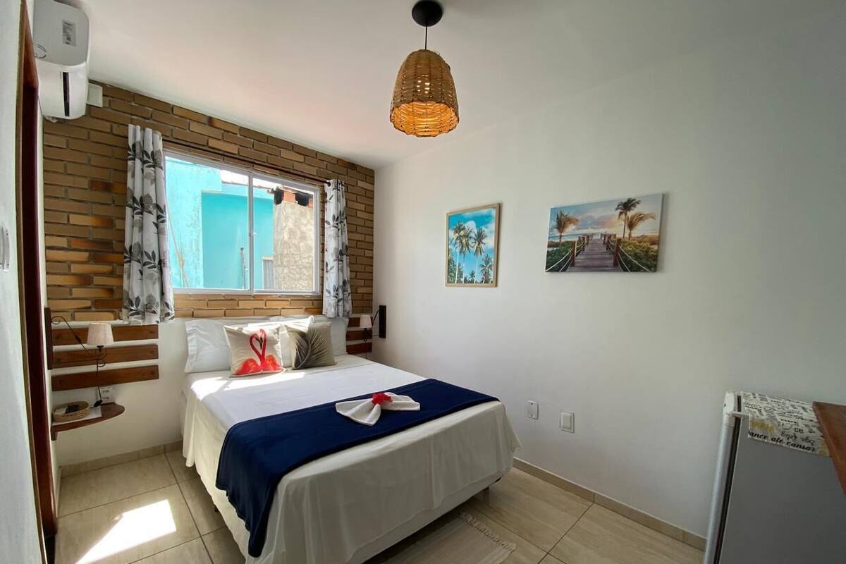 Une chambre à coucher avec un lit, une fenêtre avec des rideaux, un climatiseur fixé au mur et un luminaire au plafond.