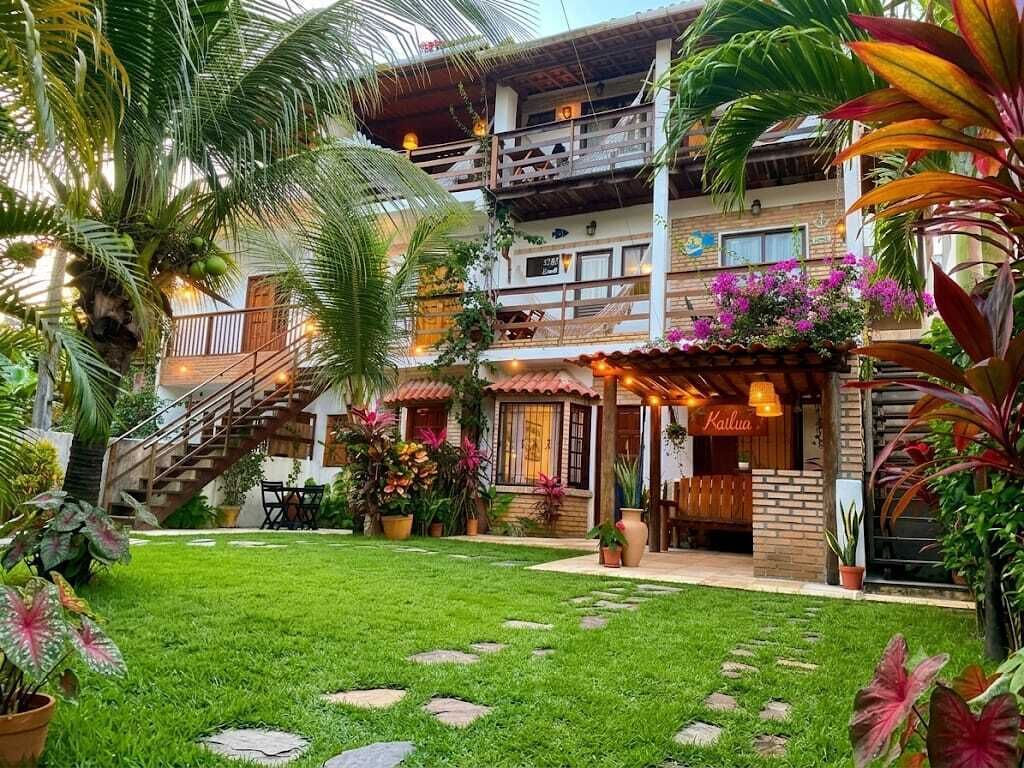 Un edificio de dos pisos con un balcón, una escalera y un jardín bien cuidado con plantas en macetas y césped.