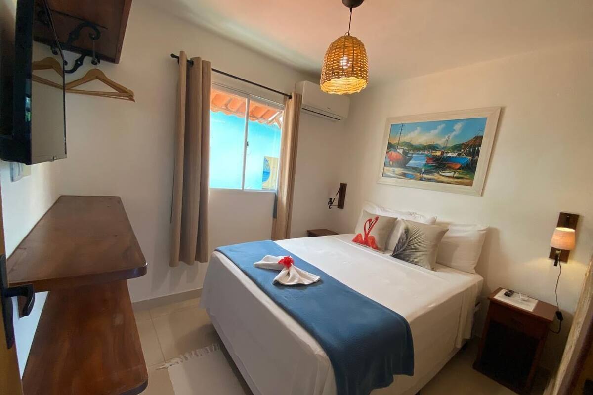 Une chambre d’hôtel avec un lit, un bureau, une chaise, une télévision, un tableau et une fenêtre avec des rideaux.