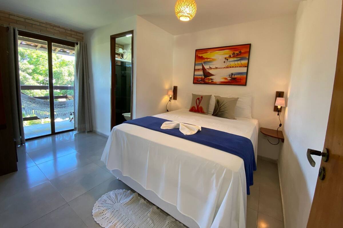 Une chambre à coucher avec un lit, un tableau, un hamac et une vue à travers une porte vitrée.