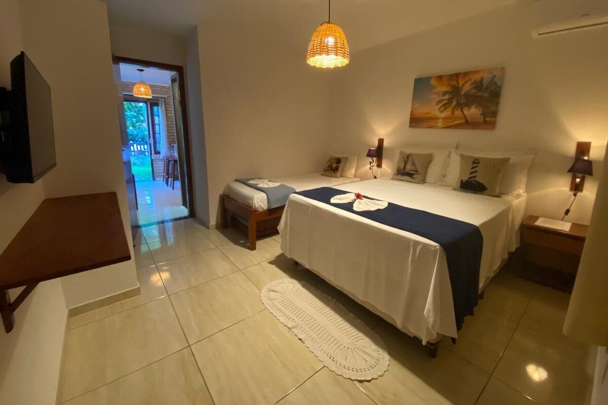 A bedroom with a bed, bedside tables, a hanging light fixture, a painting on the wall, and a view of the outside.