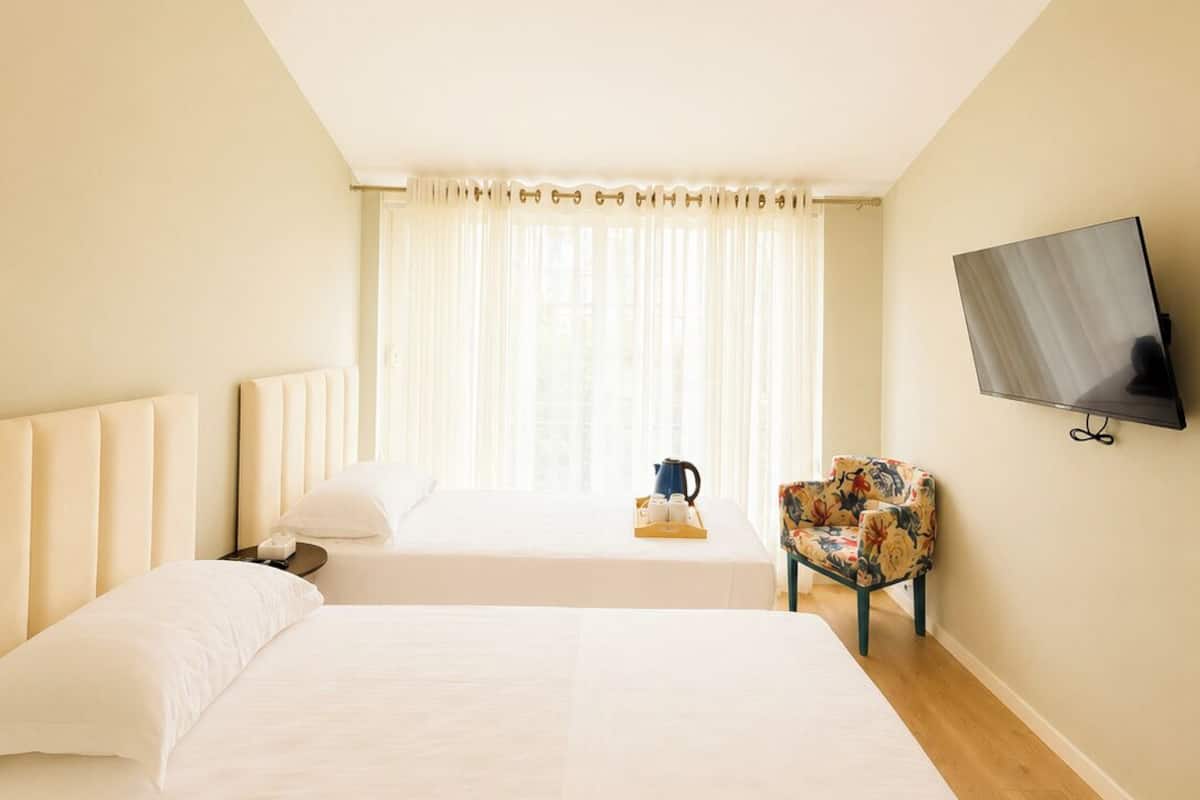 Quarto de hotel com duas camas, televisão, janela com cortinas e uma cadeira.