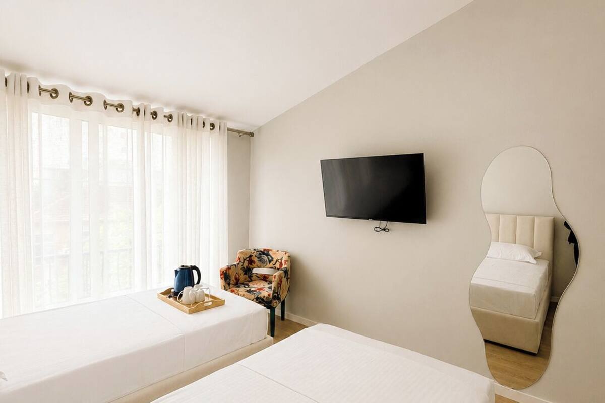 Quarto de hotel com duas camas, televisão, espelho, mesa de centro e janela com cortinas.