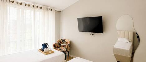 A hotel room with two beds, a TV, a mirror, a coffee table, and a window with curtains.