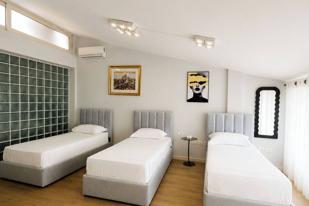 Quarto de hotel com três camas, uma janela grande e vista para a cidade.