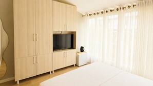A bedroom with a large bed, a TV on a wooden cabinet, a small table with a kettle, and a window with curtains. - Kein Hotel (Durres)