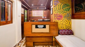 A compact room with a wooden reception desk labeled "PALETTE," a bed with a patterned pillow, a decorative wall, and a ceiling with recessed lighting.