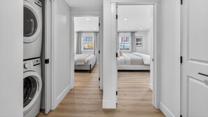 A laundry room with a washing machine, a hallway leading to two bedrooms with beds and a window, and a door to another room. - Holman's Harbourview Suite -Renovated Waterview Suite in the Heart of Summerside (Summerside)