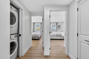 A laundry room with a washing machine, a hallway leading to two bedrooms with beds and a window, and a door to another room. - Holman's Harbourview Suite -Renovated Waterview Suite in the Heart of Summerside (Summerside)