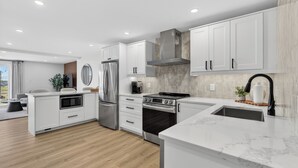 A modern kitchen with white cabinetry, stainless steel appliances, and a marble countertop. - Holman's Harbourview Suite -Renovated Waterview Suite in the Heart of Summerside (Summerside)