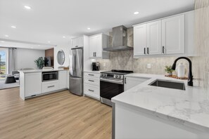 A modern kitchen with white cabinetry, stainless steel appliances, and a marble countertop. - Holman's Harbourview Suite -Renovated Waterview Suite in the Heart of Summerside (Summerside)