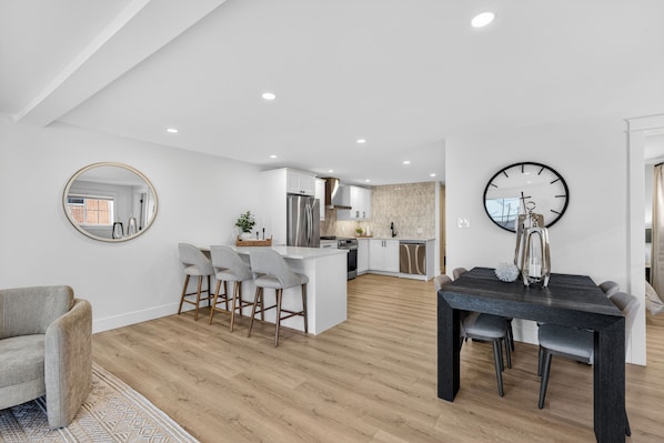 A modern kitchen with white cabinets, a central island, and a dining area with a dark table and chairs.