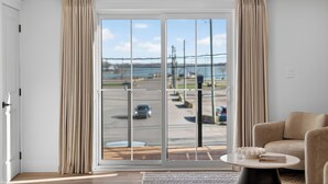 A modern room with a large sliding glass door to a parking area, a beige sofa, and a small round table. - Holman's Harbourview Suite -Renovated Waterview Suite in the Heart of Summerside (Summerside)