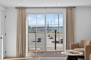 A modern room with a large sliding glass door to a parking area, a beige sofa, and a small round table. - Holman's Harbourview Suite -Renovated Waterview Suite in the Heart of Summerside (Summerside)