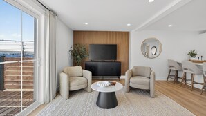 A modern living room with a large TV, two sofas, a coffee table, and a dining area with chairs. - Holman's Harbourview Suite -Renovated Waterview Suite in the Heart of Summerside (Summerside)