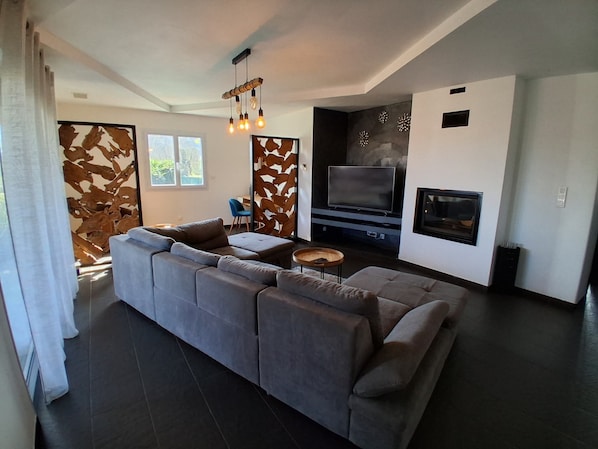 A modern living room with a sectional sofa, a flat-screen TV, a fireplace, and a decorative wall panel. - Casa Dolce vita (Talasani)