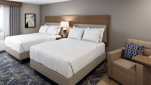 A hotel room with two beds, a nightstand, a lamp, a sofa, and a patterned rug. - Candlewood Suites Louisville Fair Expo Center by IHG (Louisville)