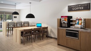 A modern coffee shop interior with a wooden table and chairs, a coffee machine, and a laptop on the table. - Candlewood Suites Louisville Fair Expo Center by IHG (Louisville)