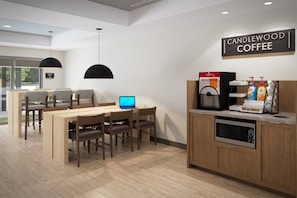 A modern coffee shop interior with a wooden table and chairs, a coffee machine, and a laptop on the table. - Candlewood Suites Louisville Fair Expo Center by IHG (Louisville)