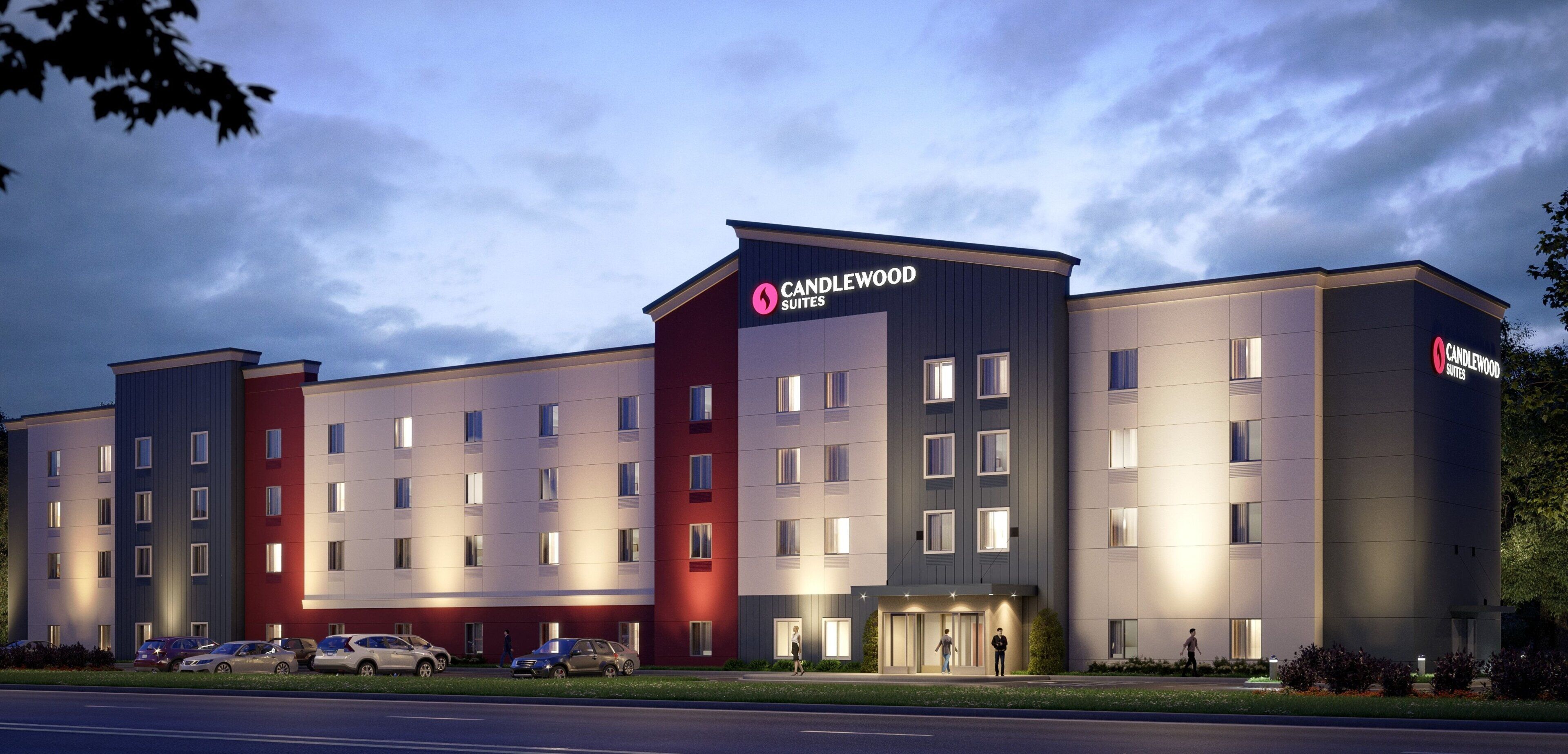 Een meerlaags hotel met een opvallend 'CANDLEWOOD SUITES' bord, met een modern architectonisch ontwerp en een combinatie van rode en grijze gevels.