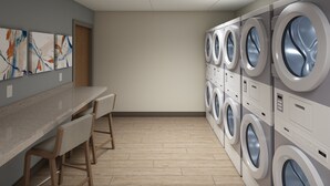 A laundry room with multiple washing machines, a wooden bench, and abstract art on the wall. - Candlewood Suites Louisville Fair Expo Center by IHG (Louisville)