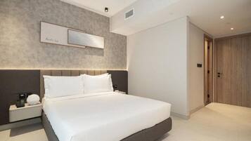 Moderni hotellihuone, jossa on suuri sänky, yöpöytä lampun kanssa ja puinen ovi.
