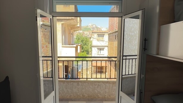 Quarto com varanda, cama e vista para edifícios.