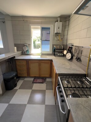 A kitchen with a gas stove, wooden cabinets, a sink, and a window with a view.