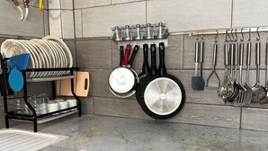 Uma cozinha com bancada de mármore, armários de madeira e diversos utensílios e panelas pendurados na parede.
