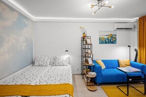 Ein Schlafzimmer mit einem Bett, einem blauen Sofa, einem Regal mit Gegenständen und einem Gemälde an der Wand.