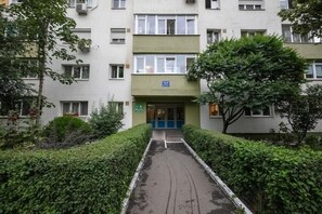Ein mehrstöckiges Gebäude mit einem zentralen Eingang, umgeben von Grünflächen und einem Weg, der zum Eingang führt.