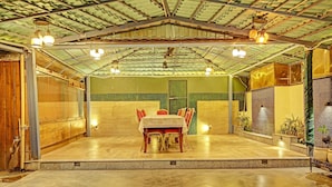 An indoor dining area with a tiled floor, a table with chairs, and a ceiling with exposed beams and hanging lights.