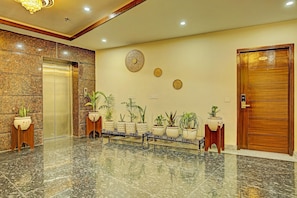A lobby with a marble floor, an elevator, potted plants, a reception desk, and a wooden door with a number plate.