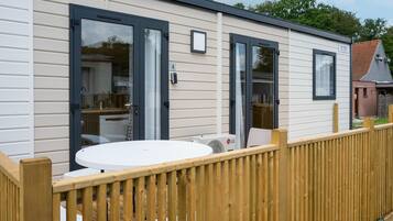 A mobile home with a deck, a round table, and a window with a view of a house.
