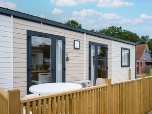 A mobile home with a deck, a round table, and a window with a view of a house. - Nice Family Caravan in the Countryside (Kaprijke)