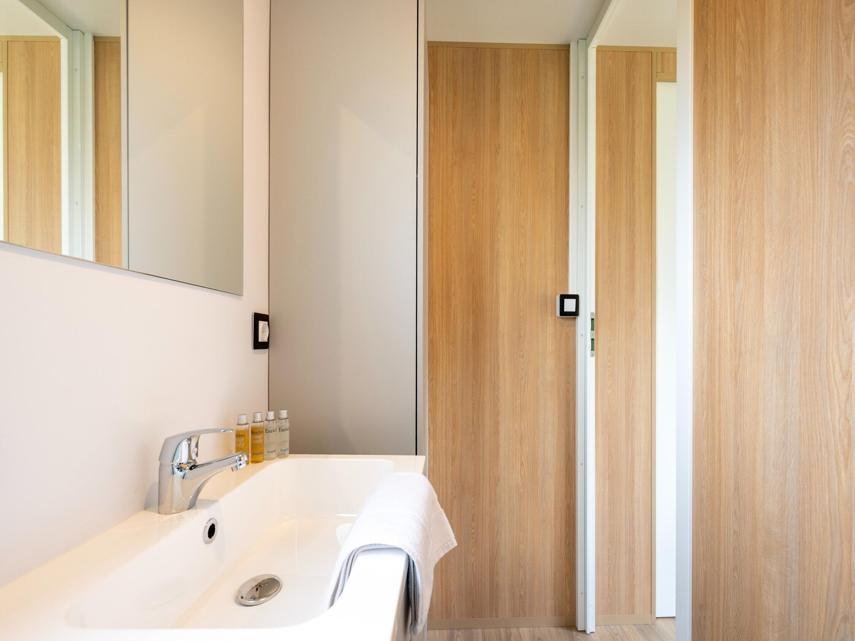 Un baño moderno con un lavabo blanco, espejo y puerta de madera.