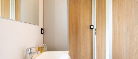 Un baño moderno con un lavabo blanco, espejo y puerta de madera.
