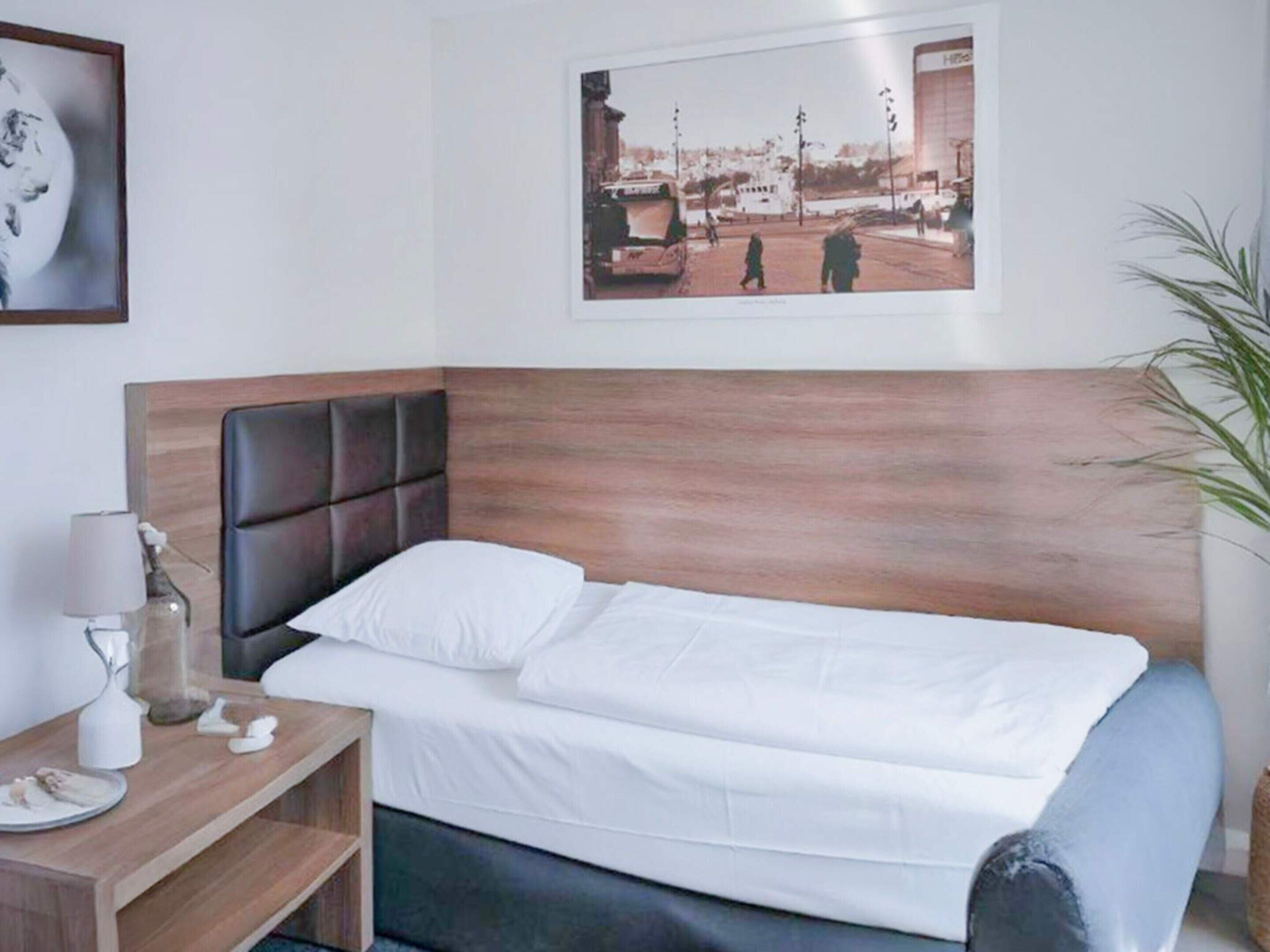 A neatly made bed with a wooden headboard, a bedside table with a lamp, and a framed picture on the wall.