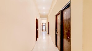 A long, narrow hallway with doors on both sides, leading to a bright room at the end. - Saver Double Hotel Parijat (Lucknow)