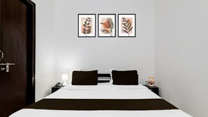 A hotel room with a bed, two bedside tables, a nightstand, a lamp, and three framed botanical prints on the wall. - Saver Double Hotel Parijat (Lucknow)