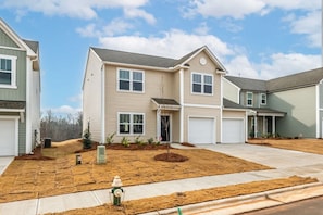 A two-story residential building with a garage, a front yard with a fire hydrant, and a clear sky. - 5BR Modern Comfort Spacious Home (Greensboro)