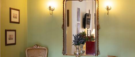 A room with a mirror, two chairs, a small table, and a red rug.