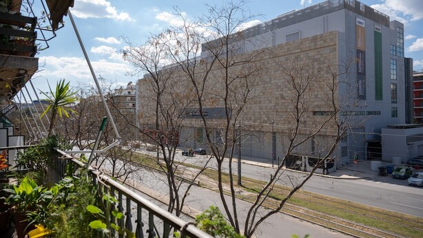 A building with a stone facade, a green vertical sign, and a clear sky. - Artline Residence in Acropolis District (Athens)