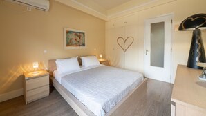 A bedroom with a bed, bedside tables, an air conditioner, a door with a heart-shaped decoration, and a lamp. - Artline Residence in Acropolis District (Athens)