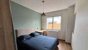 Ein Schlafzimmer mit Bett, Schreibtisch, Fenster und Heizkörper.