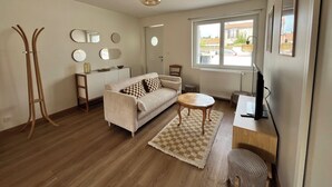 Ein Wohnzimmer mit einer Couch, einem Couchtisch, einem Fernseher, Holzboden, einem Fenster und einem Deckenventilator.