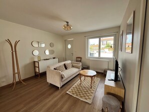 A living room with a sofa, a coffee table, a TV, a wooden floor, a window, and a ceiling fan. - Renovated house near the beaches of La Rochelle (La Rochelle)