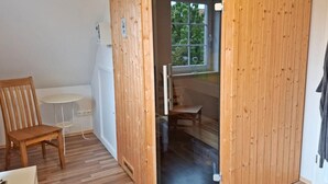 A corner room with a wooden partition, a chair, a small table, and a window with a view of greenery. - Deichhuus in Nessmersiel (Dornum)